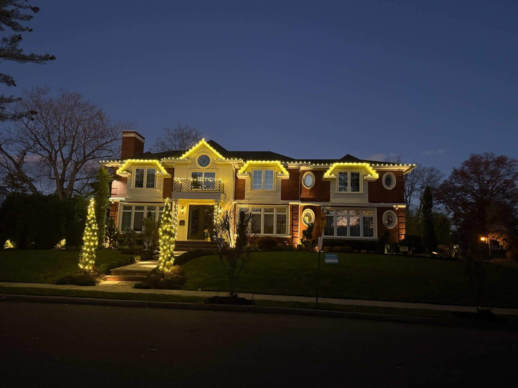 Warm-white roofline lighting and illuminated trees at a two-story home