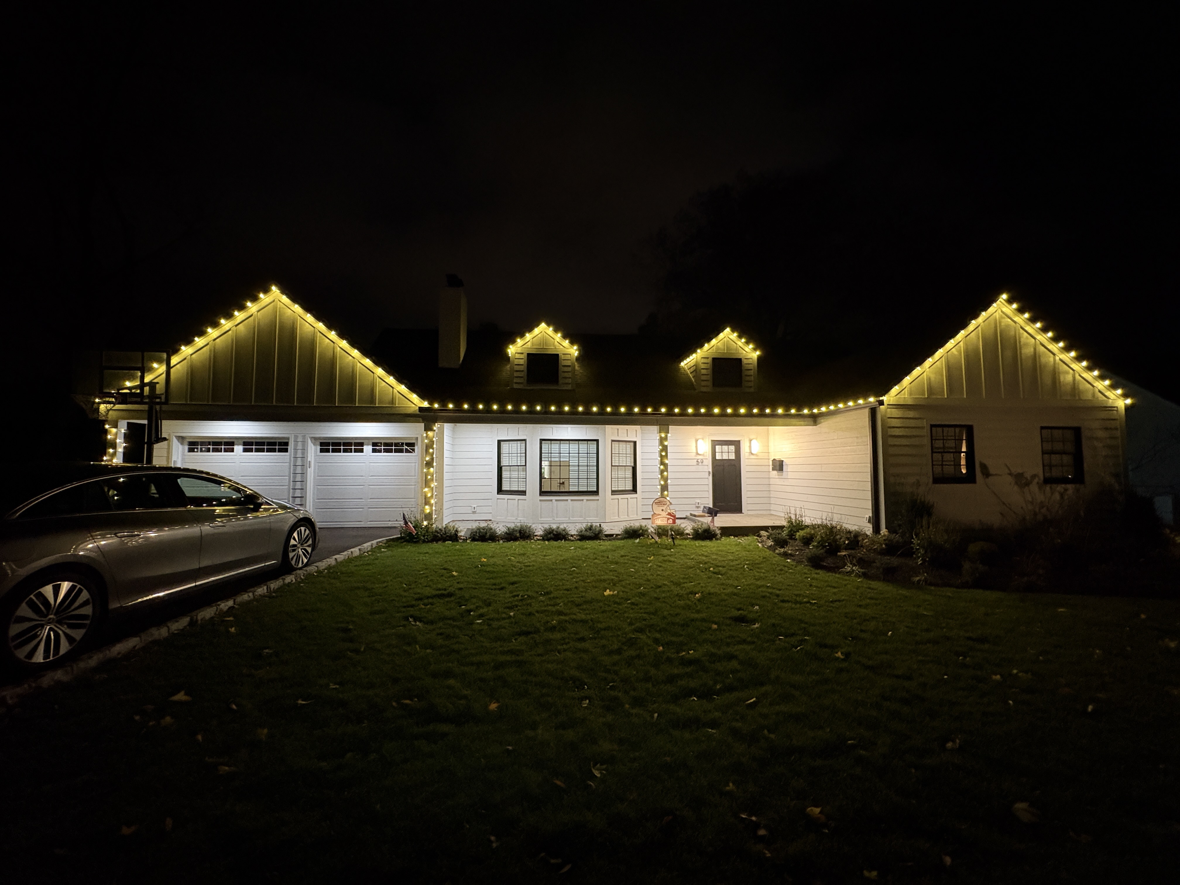 Warm-white lights tracing the gables of a white home at night