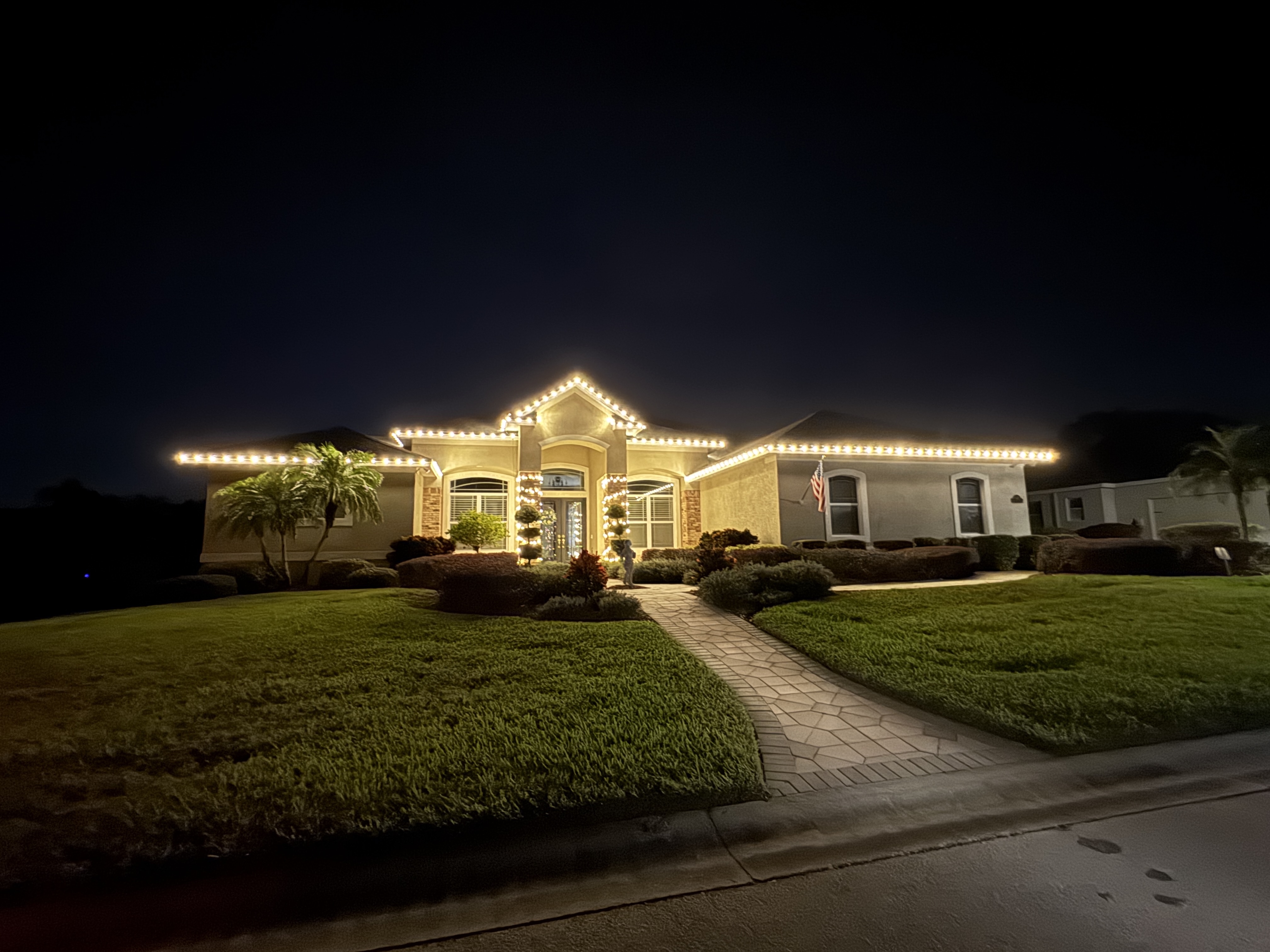 Warm-white holiday lights across a home’s roofline and entrance columns