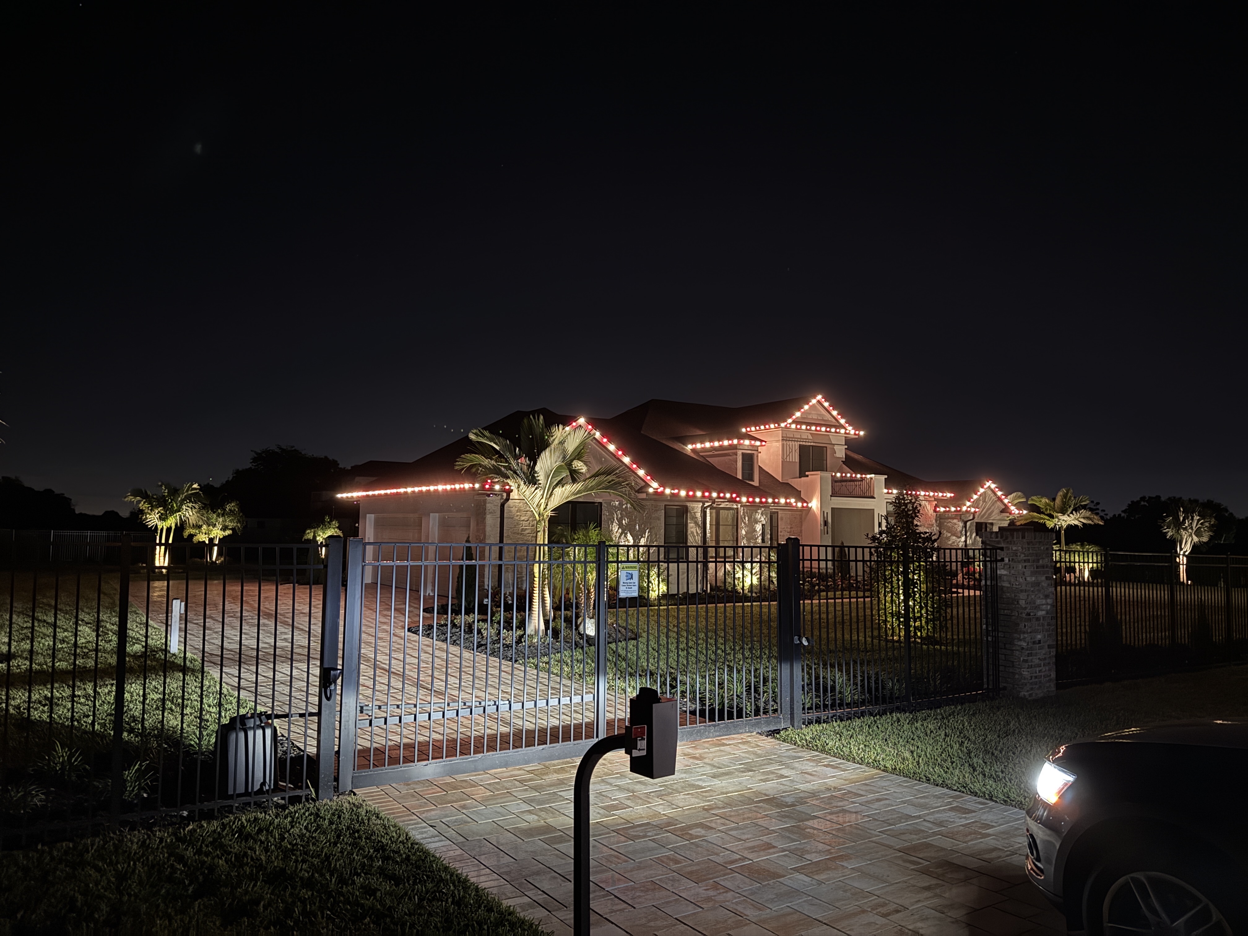 Red and white holiday lights on a two-story home behind a gated entrance