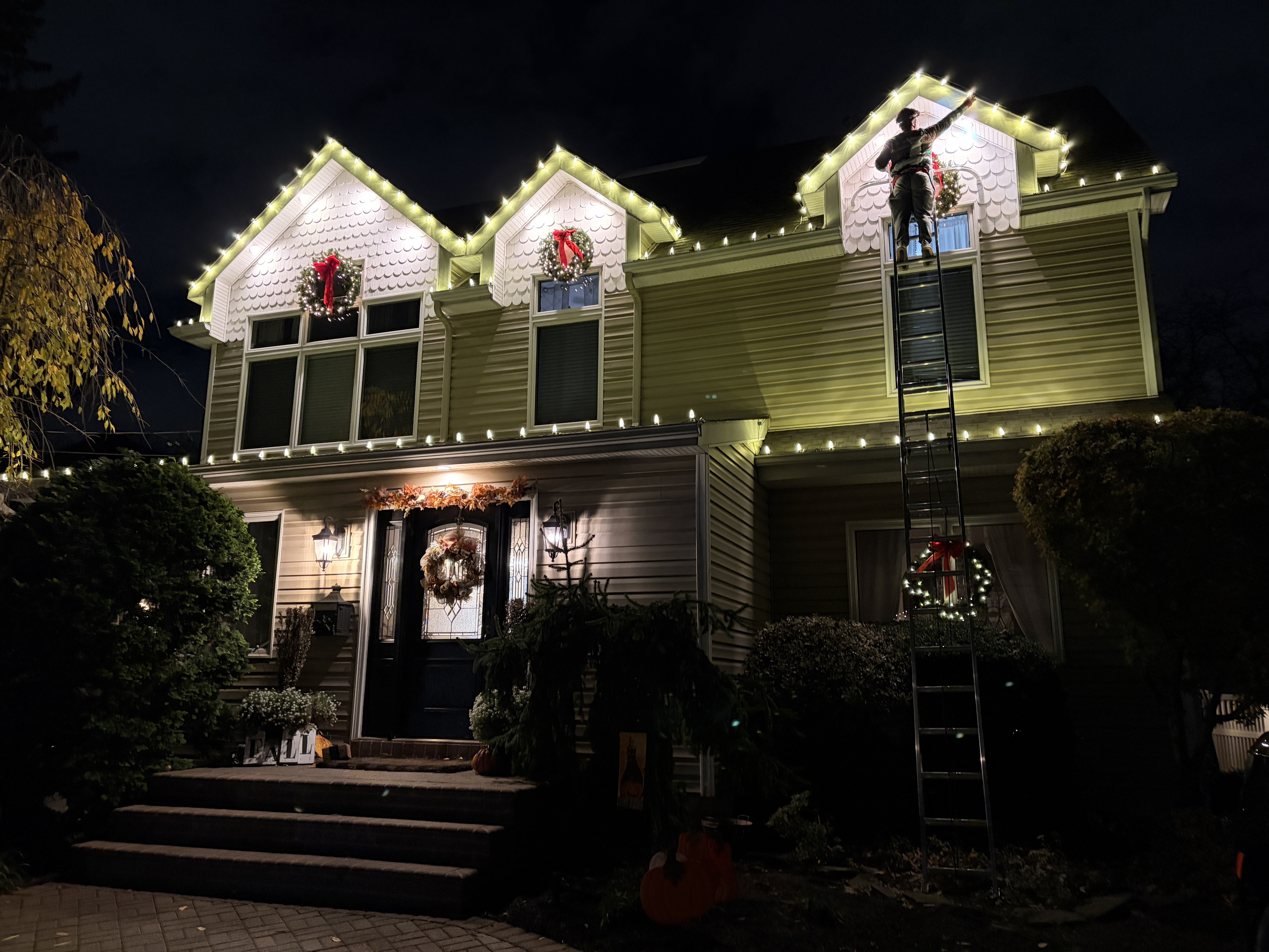 Installer on a ladder finishing roofline lights above holiday wreaths